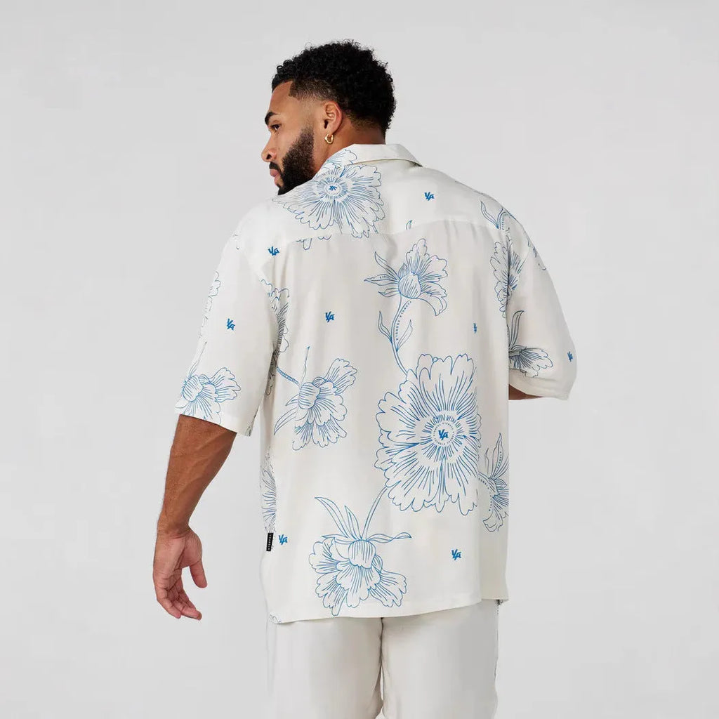 A man's loose-fitting, short-sleeve casual top with a floral print, shown in a light colour.