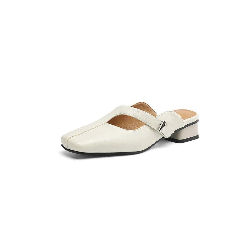 A pair of beige square head low heel slippers with a rubber sole on a wooden deck.