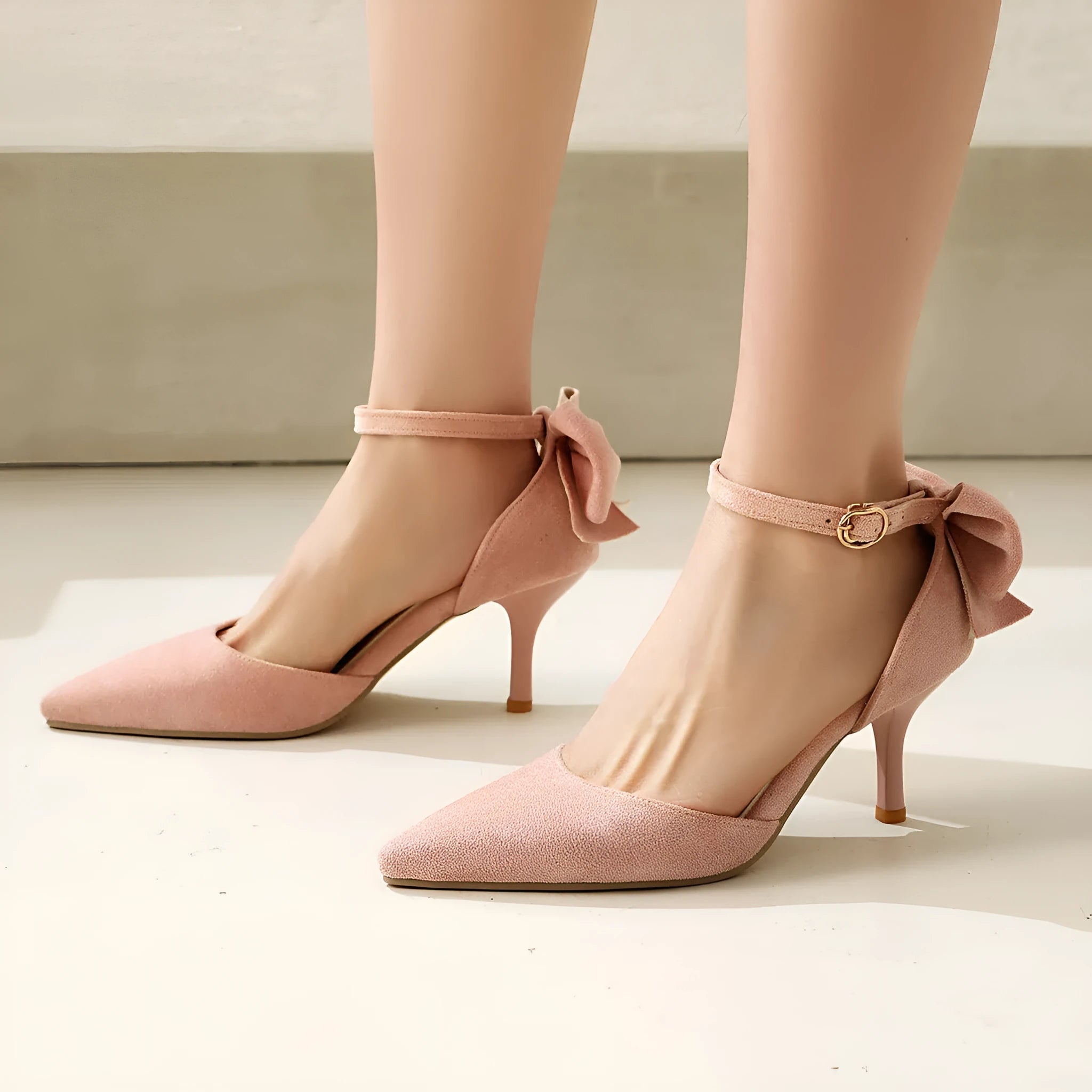 A pair of black suede stiletto high heels with a pointed toe and an ankle buckle.
