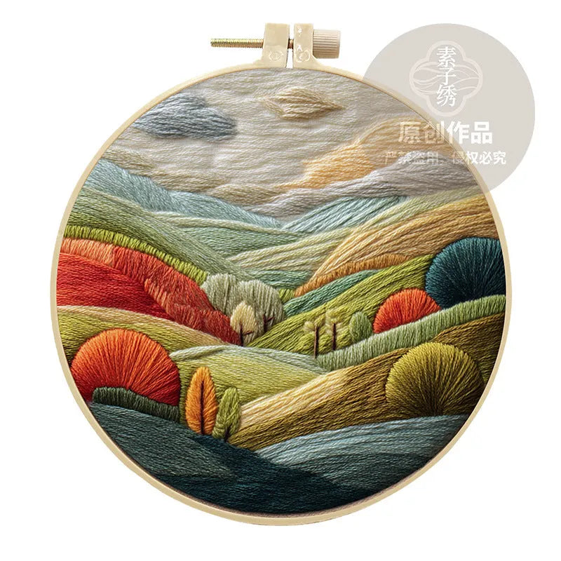 DIY embroidery kit with landscape-printed cotton fabric, embroidery hoop, needles, and coloured thread spools.
